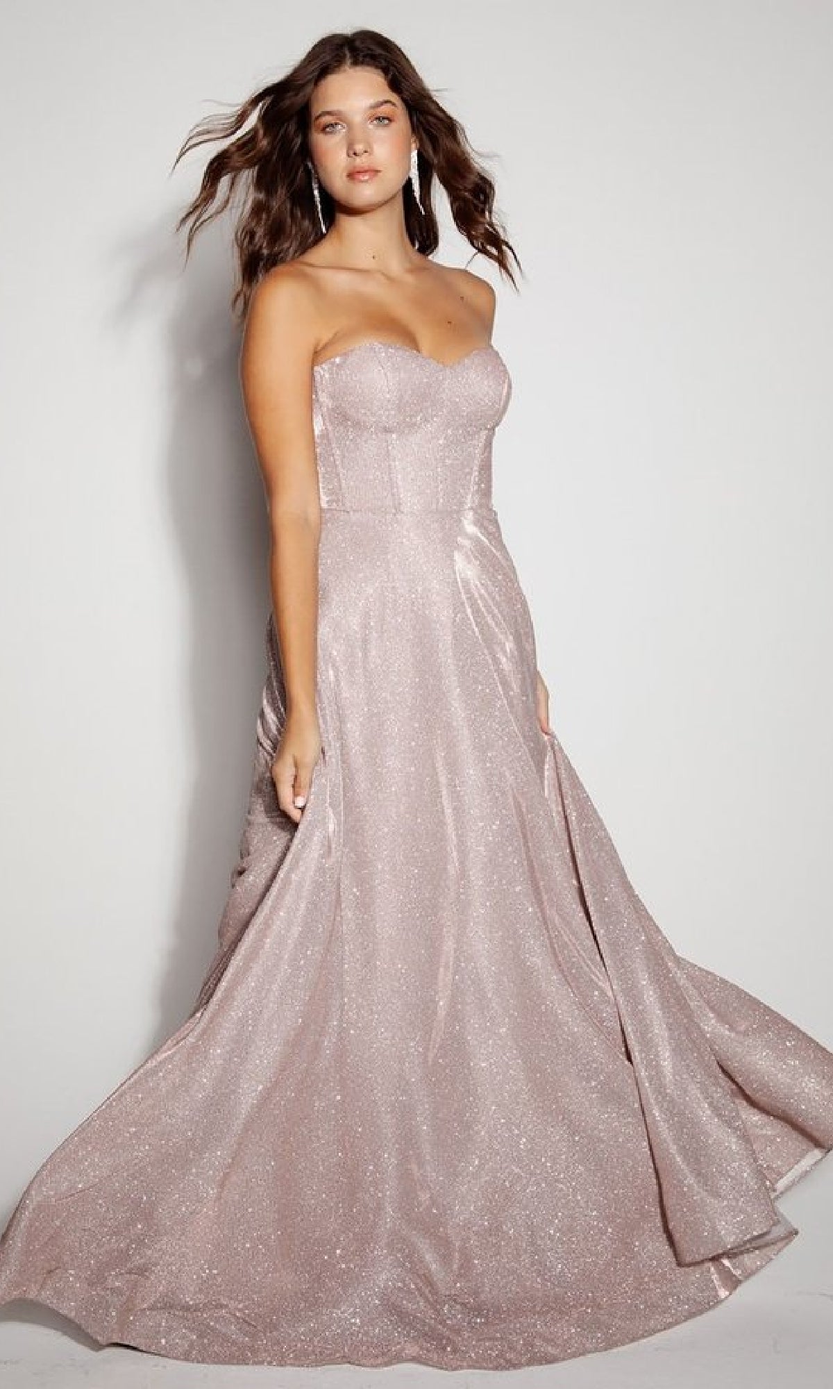 A woman stands against a plain background wearing the Eureka 9878 Lace-Up Long Glitter Prom Dress, featuring a floor-length light pink design and a sweetheart corset-style bodice.